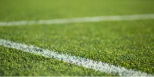 Close-up of green artificial turf with a white football pitch line, from Game On Turf; crisp texture of the grass and a sharp boundary mark visible.
