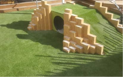 Green artificial turf playground with tan brick climbing structures installed by GameOn Turf at Matamata Intermediate School in New Zealand, for a multi-sport outdoor area.