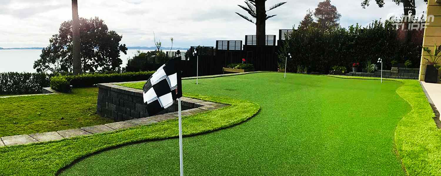 Artificial grass putting green with flags and a checkered marker on a sunny day.